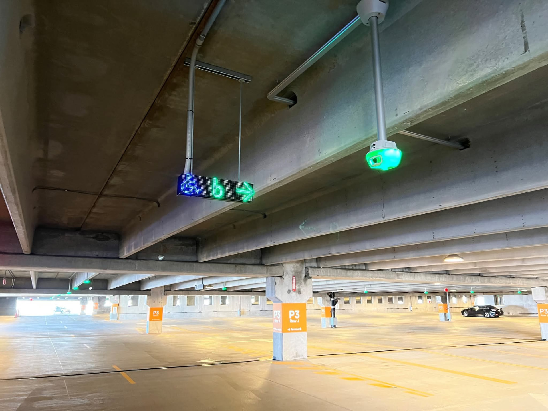 Suspended LED directional sign and occupancy sensor mounted to a parking garage deck